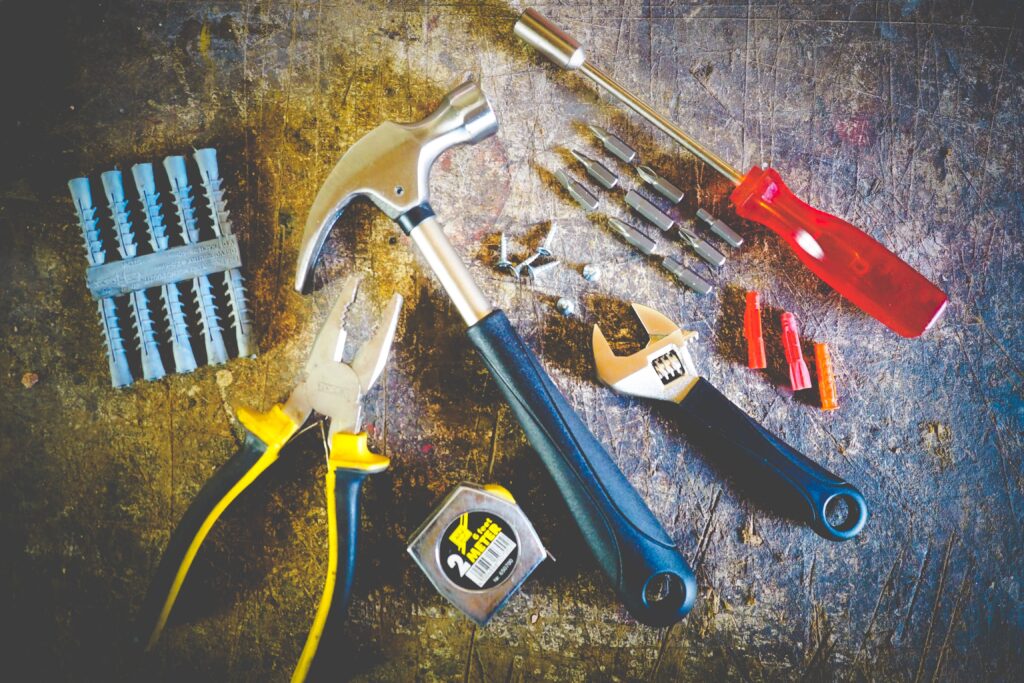 Miscellaneous tools for rental property maintenance. It includes plyers, a hammer, a wrench, measuring tape, and various screwdriver pieces.