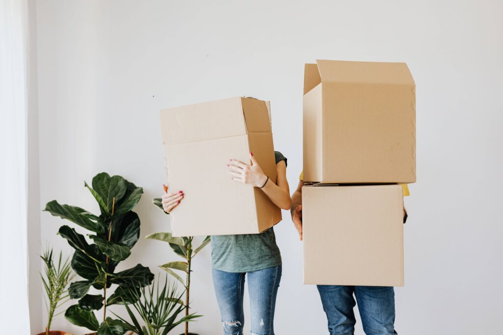 Two tenants hold boxes as they move into a new rental home. This represents that property managers help fill rental homes with tenants that are a good fit.